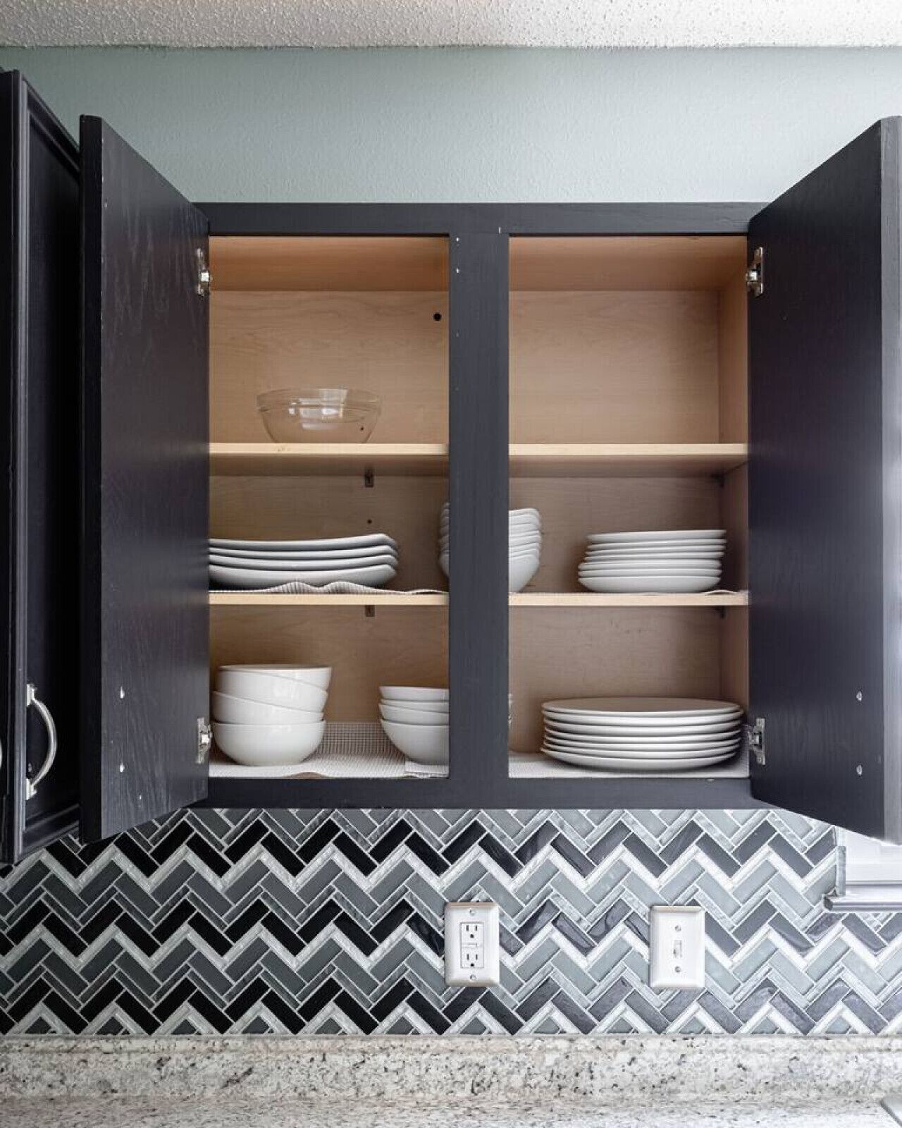 Un mueble de cocina con puertas abiertas, mostrando repisas con platos y cuencos apilados.