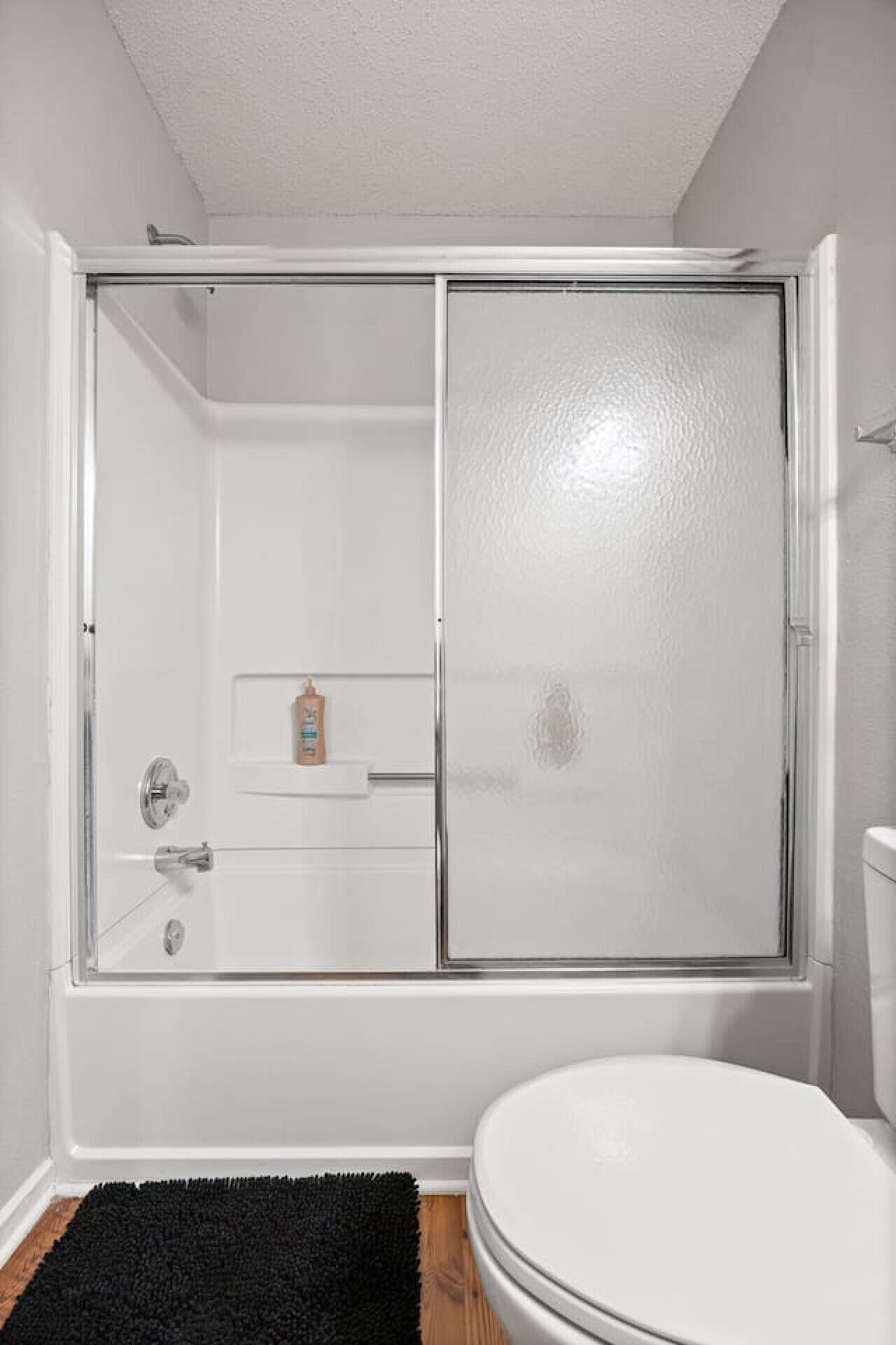 A bathroom with a shower, toilet, and a small shelf with toiletries.