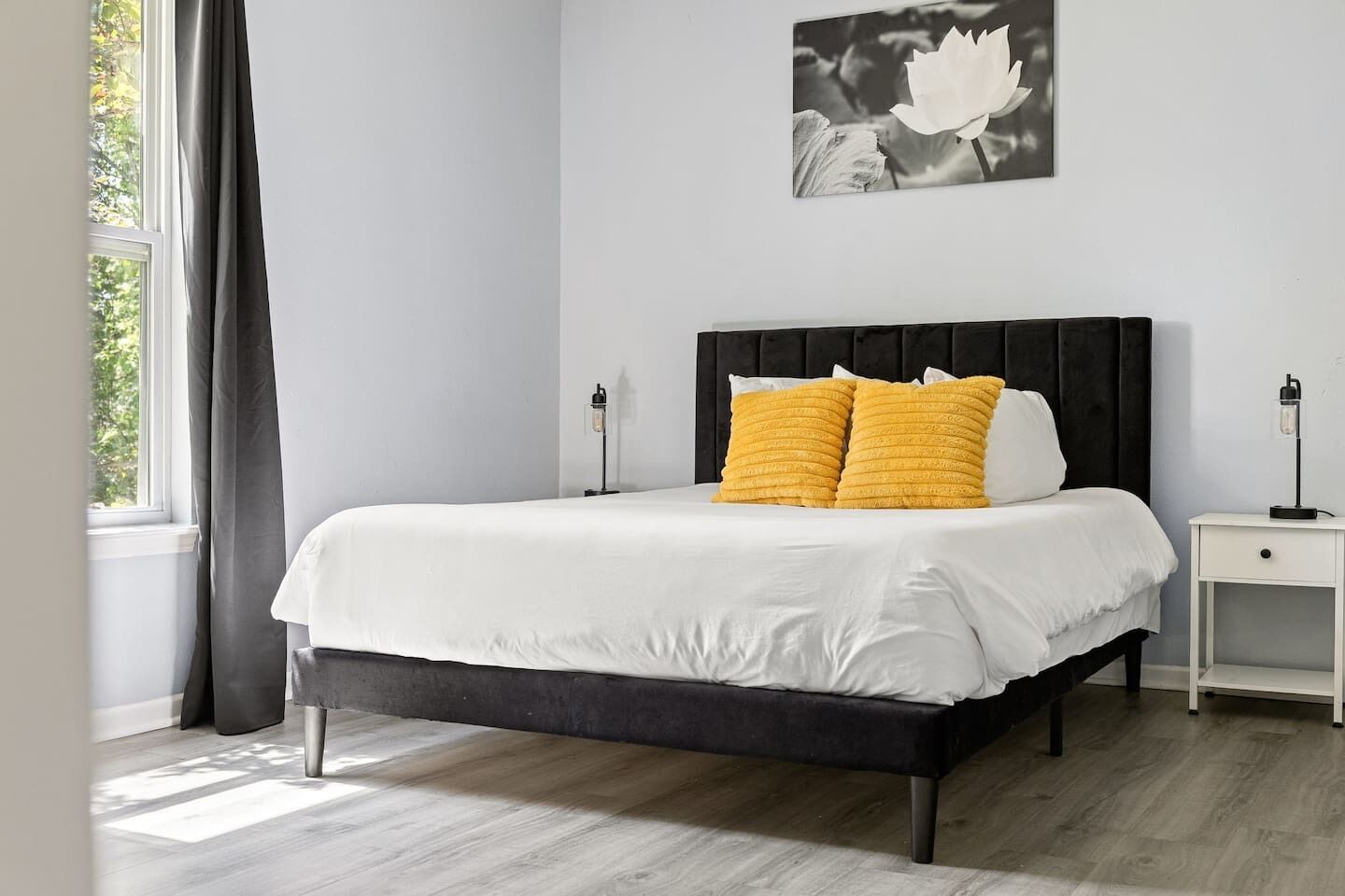 Ein Schlafzimmer mit einem Bett, zwei Nachttischen, einem Fenster mit Vorhängen und einem Wandbild.