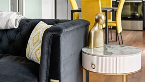 Ein modernes Wohnzimmer mit einem schwarzen Sofa, einem runden Beistelltisch mit Marmorplatte und einem gelben Sessel im Hintergrund.