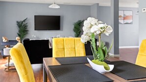 Ein modernes Wohnzimmer mit einer Couch, gelben Sesseln, einem Esstisch mit schwarzem Läufer und einem an der Wand befestigten Fernseher.