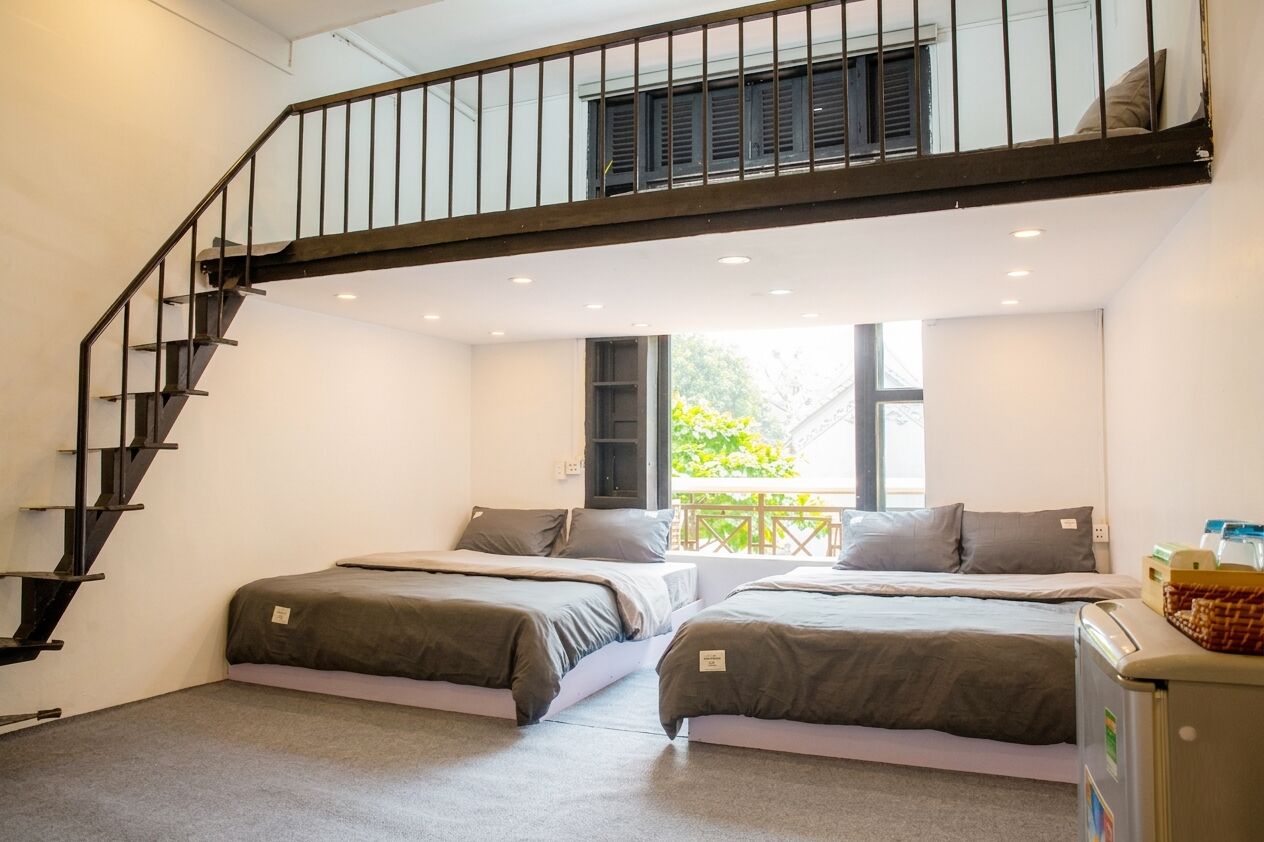 A room with two beds, a staircase, a window, and a small kitchenette.