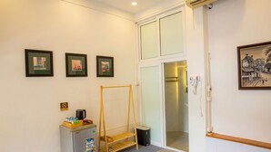 A hotel room with a bed, a small refrigerator, a wooden shelf, a door with a glass panel, and framed pictures on the wall. - Hoan Kiem Lake View / Balcony / 3Q Beds / 6 Pax (Hà Nội)