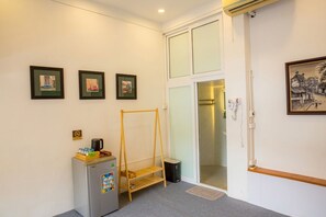 Ett hotellrum med en säng, ett litet kylskåp, en hylla i trä, en dörr med ett glasparti och inramade tavlor på väggen.