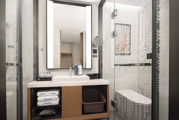 A modern bathroom with a glass shower enclosure, a white sink with a mirror above, and a wooden vanity with towels and toiletries. - Hampton by Hilton Guangzhou Changlong Wanbo Center - Free Shuttle Bus During the Canton Fair (Guangzhou)