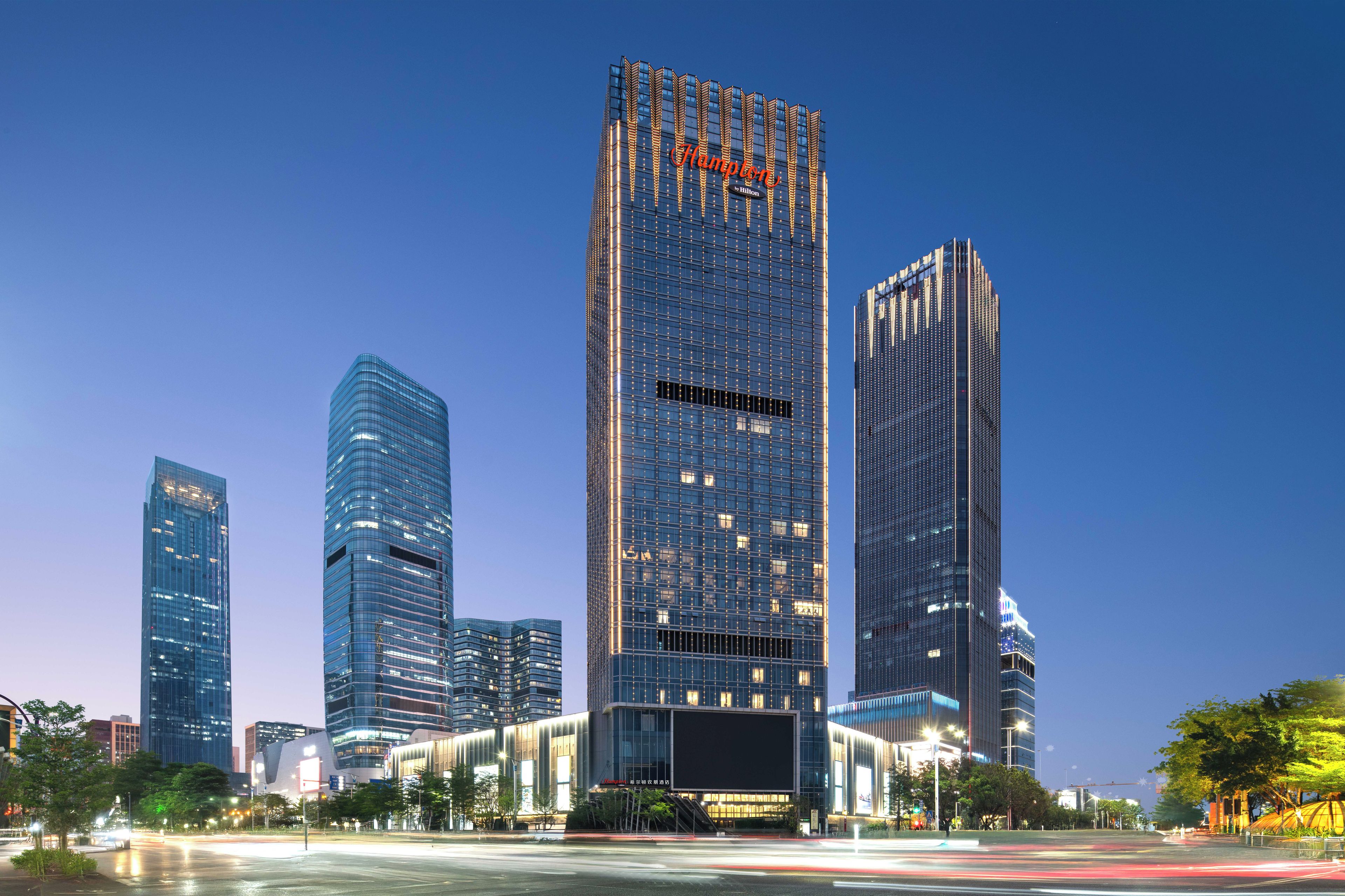 Un edificio moderno de gran altura con un letrero llamativo, rodeado de otros edificios altos en un paisaje urbano.