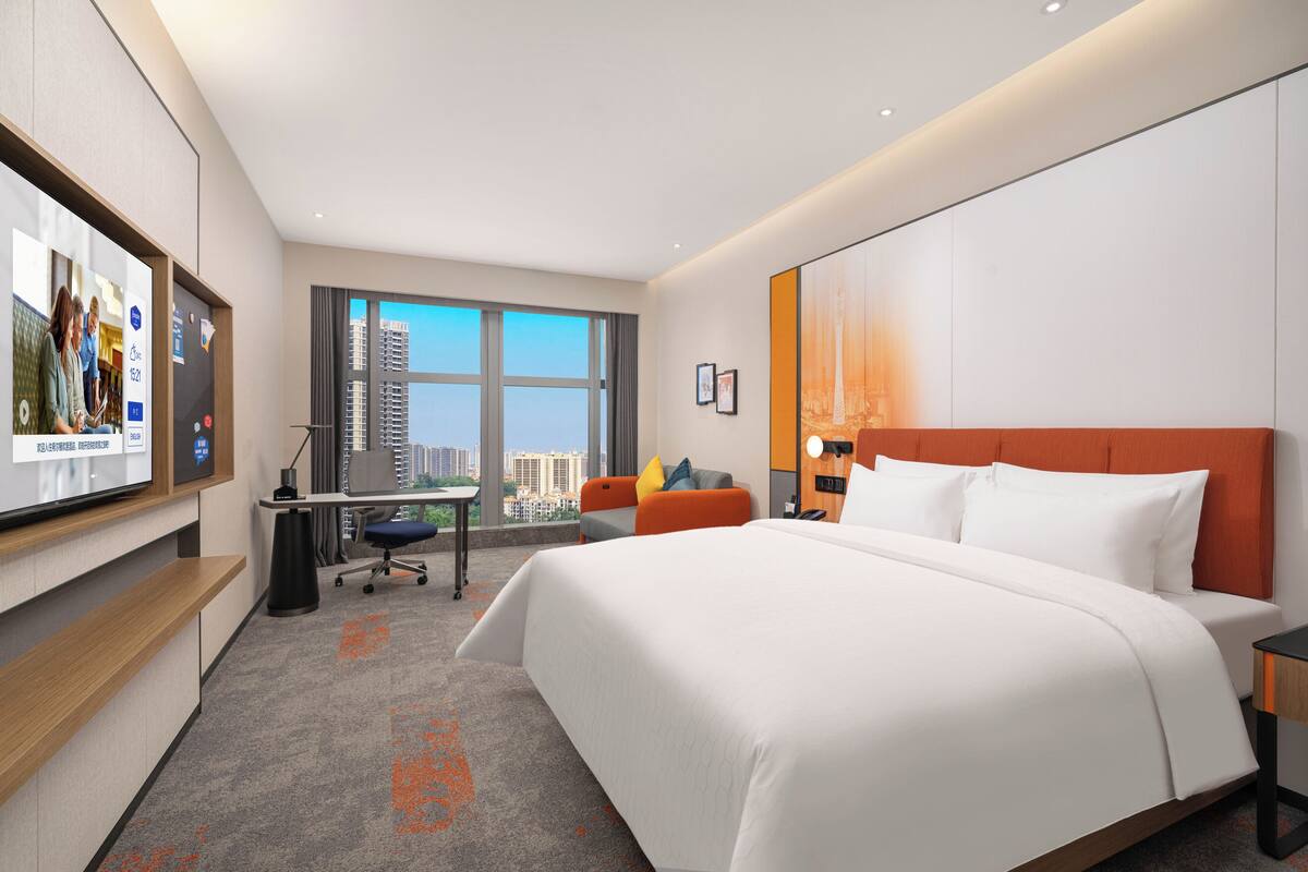 Habitación de hotel con una cama grande, un escritorio, una silla y un televisor en la pared.