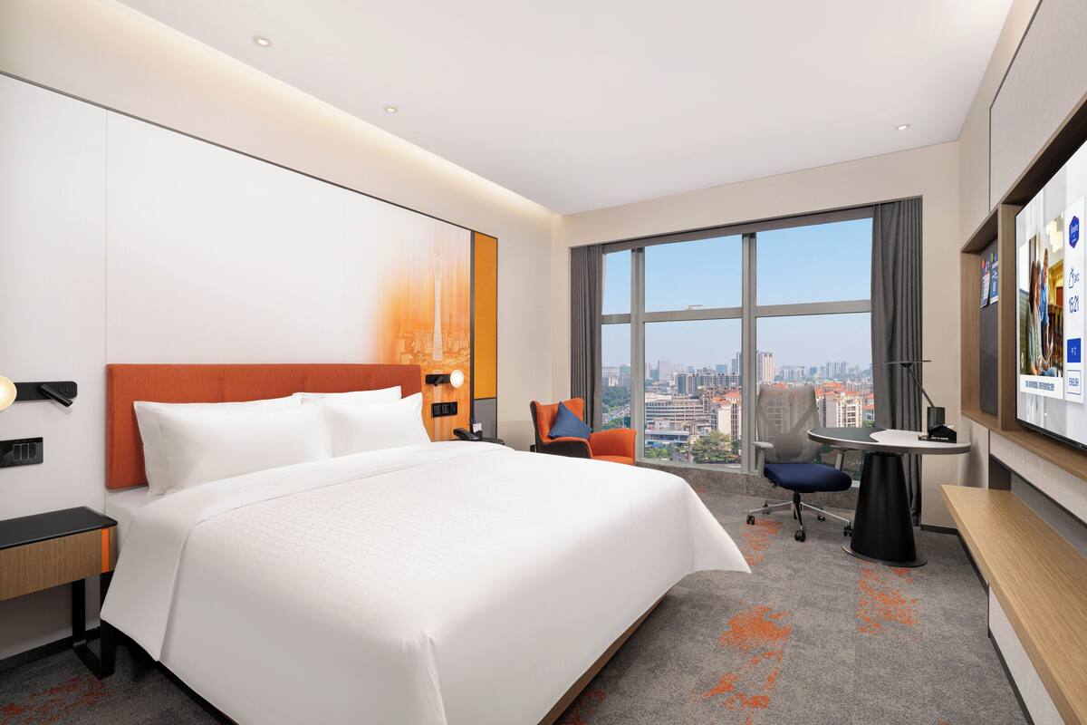 Habitación de hotel con una cama grande, un escritorio, una silla, un televisor y vistas a la ciudad.