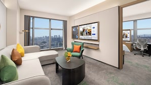 Et moderne hotelværelse med et stort vindue, en sofa, et sofabord, et fjernsyn og et skrivebord med kontorstole.