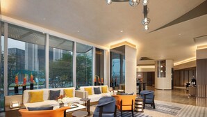 En moderne hotellobby med sofa, stole, et sofabord og store vinduer med udsigt over byen.
