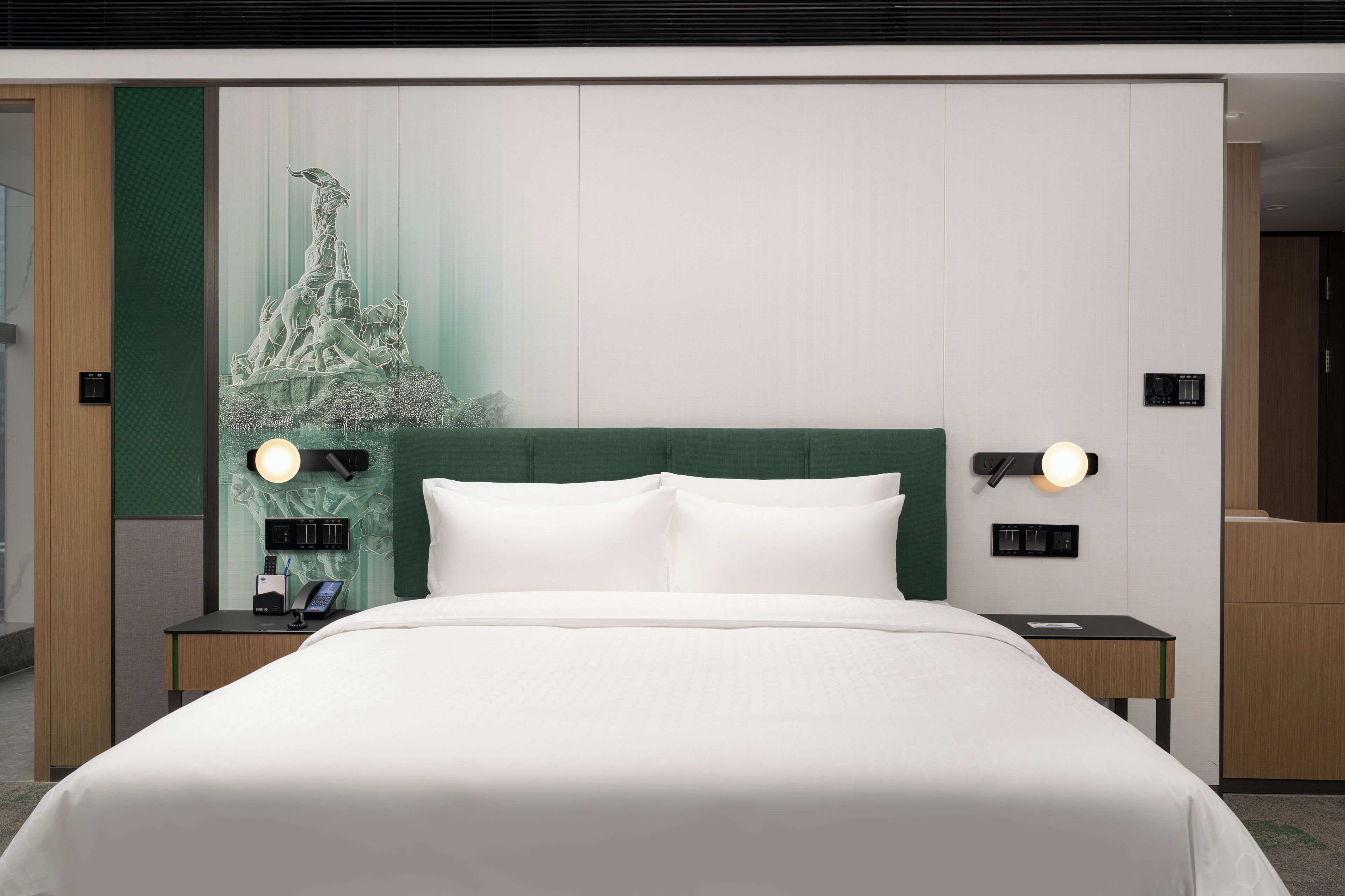 A modern hotel room with a large bed, two bedside tables, a green headboard, and a wall-mounted light fixture.