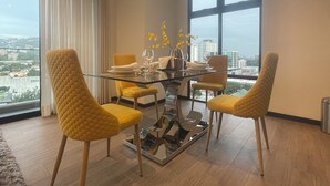 Un comedor con una mesa de vidrio, sillas amarillas, un jarrón con flores amarillas y vistas de la ciudad a través de amplias ventanas.