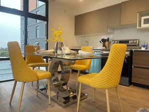 A modern dining area with a glass table, yellow chairs, and a vase of yellow flowers. - Luxurious Apt. Z.10 GT City | 2Bedroom | AC | Wifi | Parking | Swimming Pool Jacuzzi (Ciudad de Guatemala)