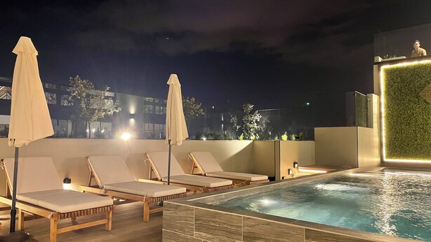 Un área de piscina en la azotea con sillones de descanso y sombrillas, una piscina pequeña y un muro cubierto de vegetación.