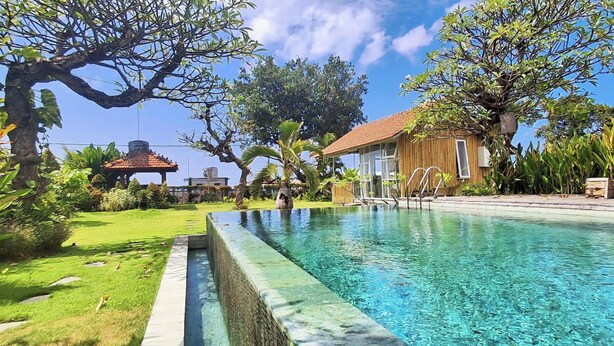A swimming pool with a wooden deck, surrounded by lush greenery and a clear blue sky.