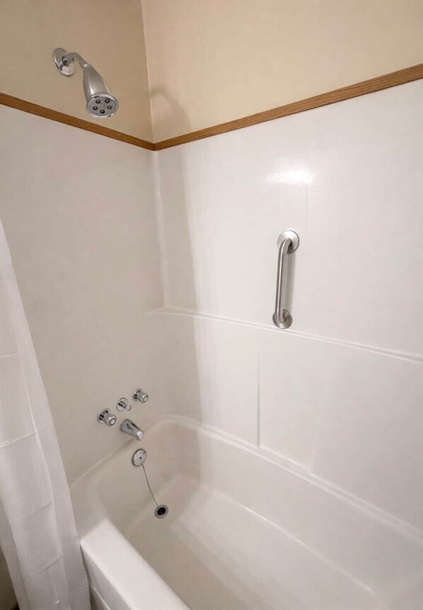 A bathroom with a bathtub, a showerhead, and a handrail.