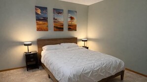 A bedroom with a wooden bed, two bedside tables, and three wall-mounted paintings.