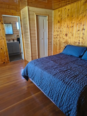 Una stanza con pannelli in legno, un letto, una porta che dà su un bagno e un angolo con lavandino.