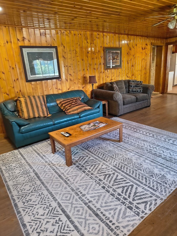 A wooden-paneled room with two sofas, a patterned rug, and framed pictures on the wall.