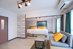 Une chambre d’hôtel moderne avec un lit, un canapé, un plancher en bois, un mur en pierre et une fenêtre avec des rideaux.