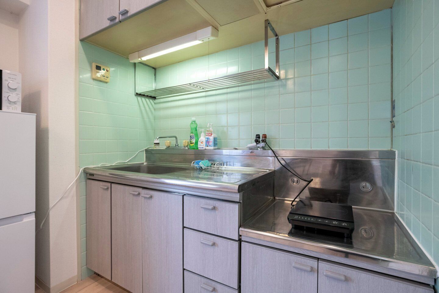 Una cocina con un lavamanos de acero inoxidable, una campana extractora y paredes con azulejos verde claro.