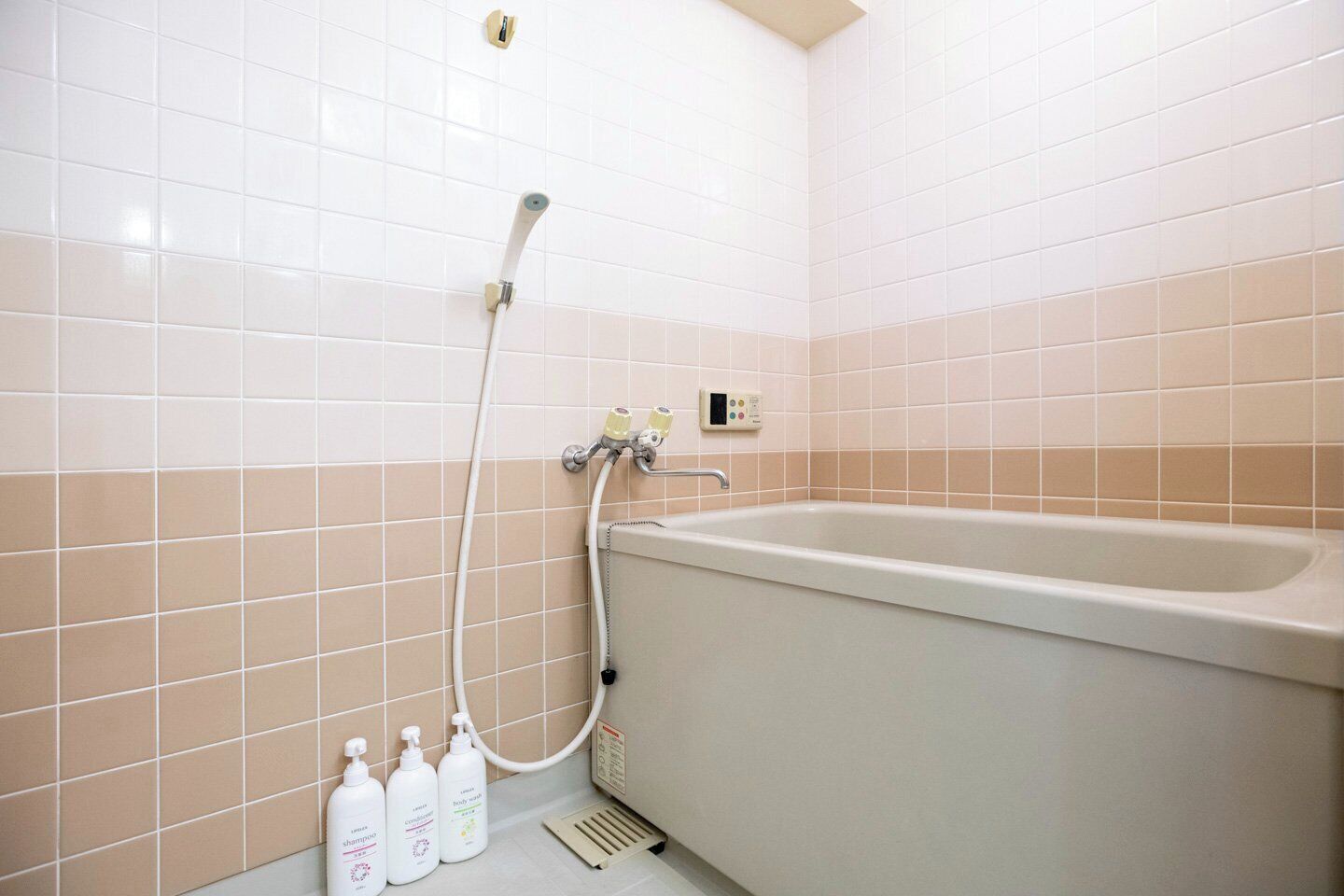 A bathroom with a bathtub, a handheld showerhead, and three bottles of shampoo.