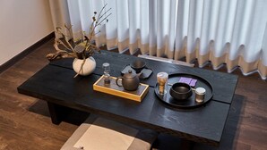 Un tavolo di legno con un servizio da tè, un vaso con rami e un cuscino.