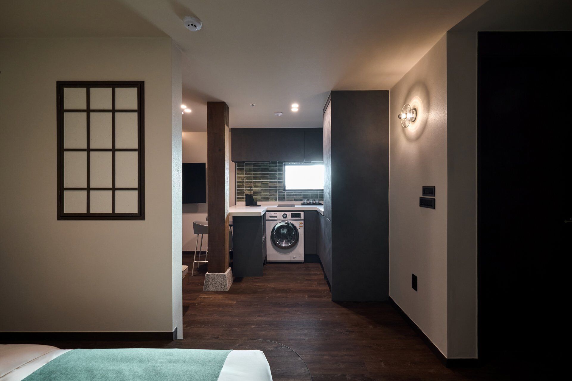 Habitación de hotel moderna con cama, una pequeña zona de estar, lavadora y cocina con ventana.