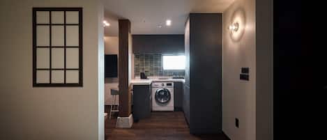 Habitación de hotel moderna con cama, una pequeña zona de estar, lavadora y cocina con ventana.