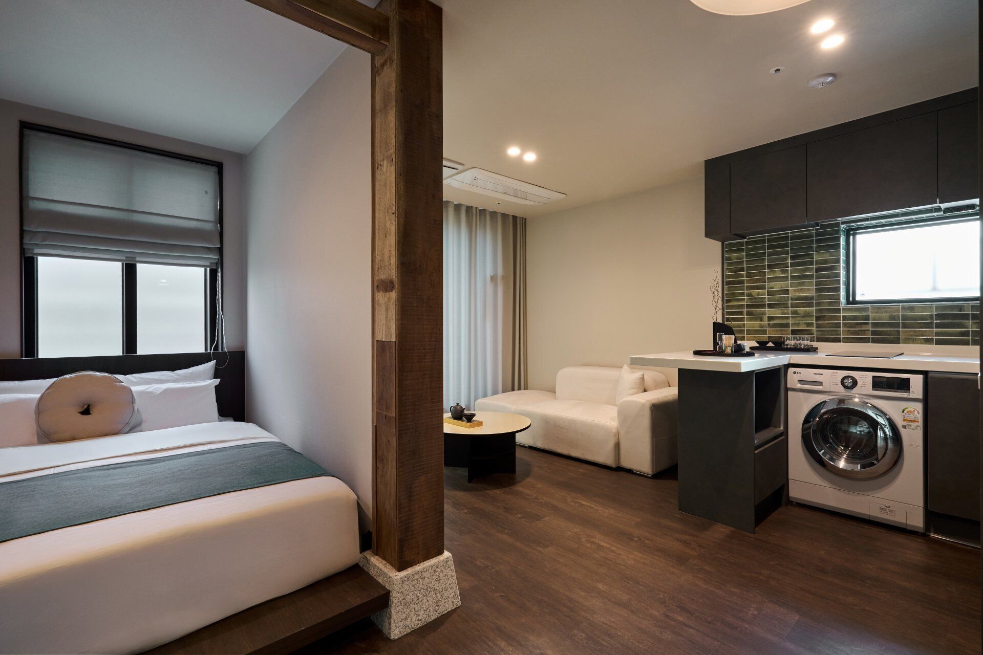 Una habitación de hotel compacta con una cama, un pequeño rincón de descanso, una lavadora y una kitchenette.