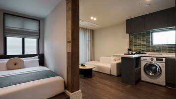 Una habitación de hotel compacta con una cama, un pequeño rincón de descanso, una lavadora y una kitchenette.