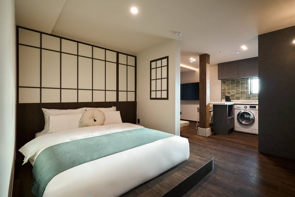 Une chambre avec un grand lit, un lave-linge et une petite kitchenette.