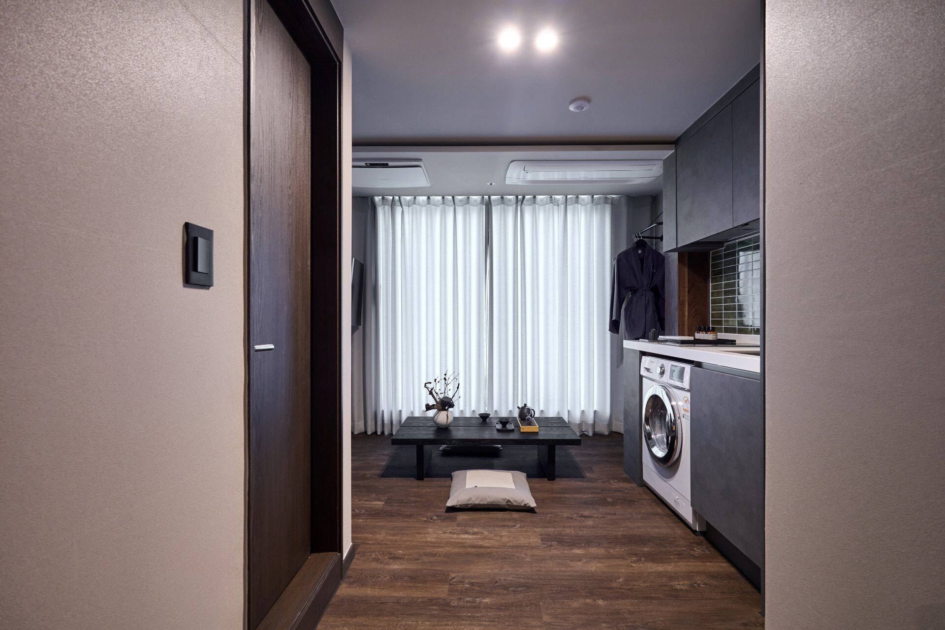 A modern kitchen with a washing machine, a dining area with a table and chairs, and a view of the outside through a window with curtains.