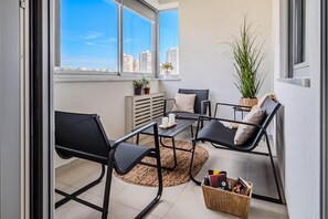 Un balcón con zona de estar, que incluye dos sillas, una mesa, una planta en maceta y una cesta con objetos.