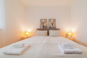 Hotellihuone, jossa on suuri sänky, kaksi yöpöytää lamppuineen ja kaksi seinälle ripustettua taulua.