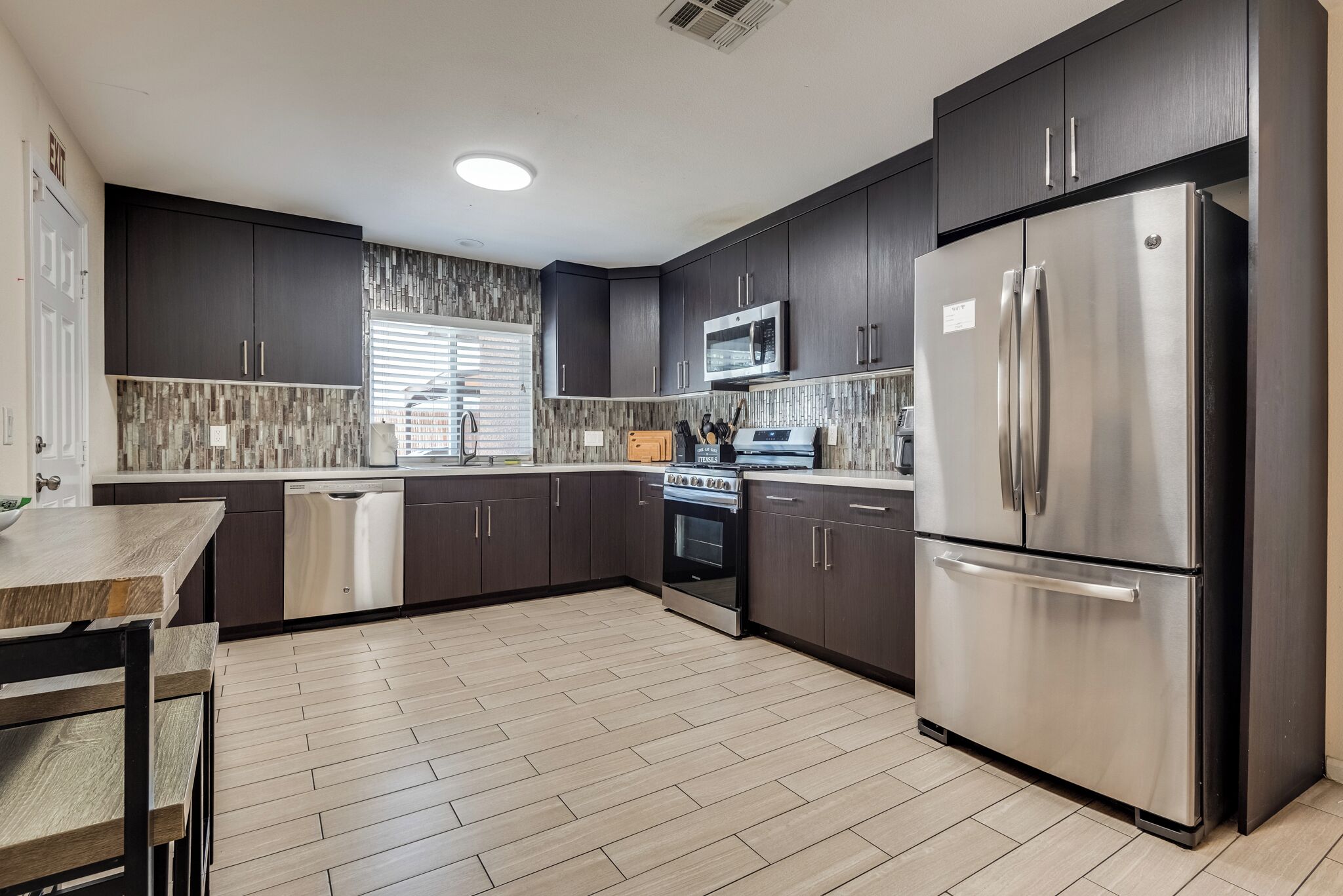 A modern kitchen with dark cabinetry, stainless appliances, and a herringbone-patterned backsplash.