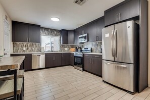 A modern kitchen with dark cabinetry, stainless appliances, and a herringbone-patterned backsplash. - Lux - Mins To Strip, Allegiant Stadium and The Sphere (Las Vegas)