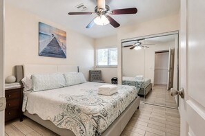 A bedroom with a bed, a nightstand, a chair, a ceiling fan, a large mirror, and a painting on the wall. - Hot Tub + Pool - 10 Min to Strip - Fire Pit & Games (Las Vegas)