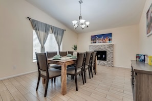 A dining area with a wooden table and chairs, a chandelier, a fireplace, and a cityscape painting on the wall. - Lux - Mins To Strip, Allegiant Stadium and The Sphere (Las Vegas)