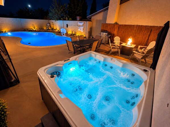 Uma banheira de hidromassagem com água borbulhante, piscina, mobiliário de exterior e lareira.
