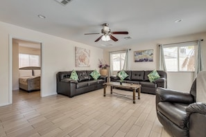 A living room with a dark leather sofa, a wooden coffee table, a ceiling fan, and a large window with curtains. - Lux - Mins To Strip, Allegiant Stadium and The Sphere (Las Vegas)