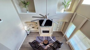 Un salon moderne avec un canapé d’angle, une cheminée, un ventilateur de plafond et des plantes en pot.