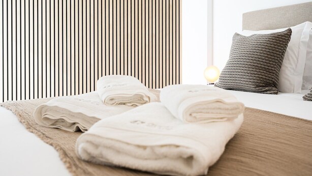 Un lit bien fait, avec des serviettes pliées, un plaid à motifs et un coussin décoratif.
