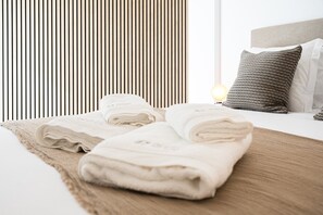 Una cama bien hecha con toallas dobladas, un plaid con textura y una almohada estampada.