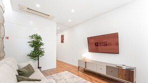 Un salon moderne avec un canapé, une plante, un téléviseur et une console au design minimaliste.