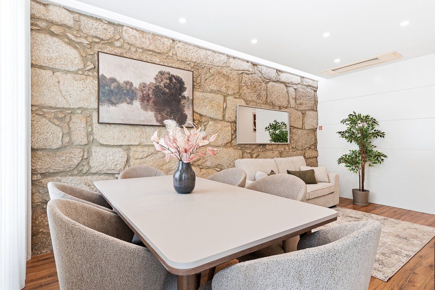 A dining area with a stone wall, a painting, a vase with flowers, a sofa, and a potted plant.
