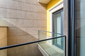 A balcony with a glass railing, a window with curtains, and a textured wall. - GuestReady - Blossom Mosaic Marigold Apartment (Porto)