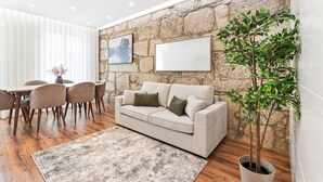 Un salon avec un mur en pierre, un canapé, une table à manger avec des chaises et une plante en pot.