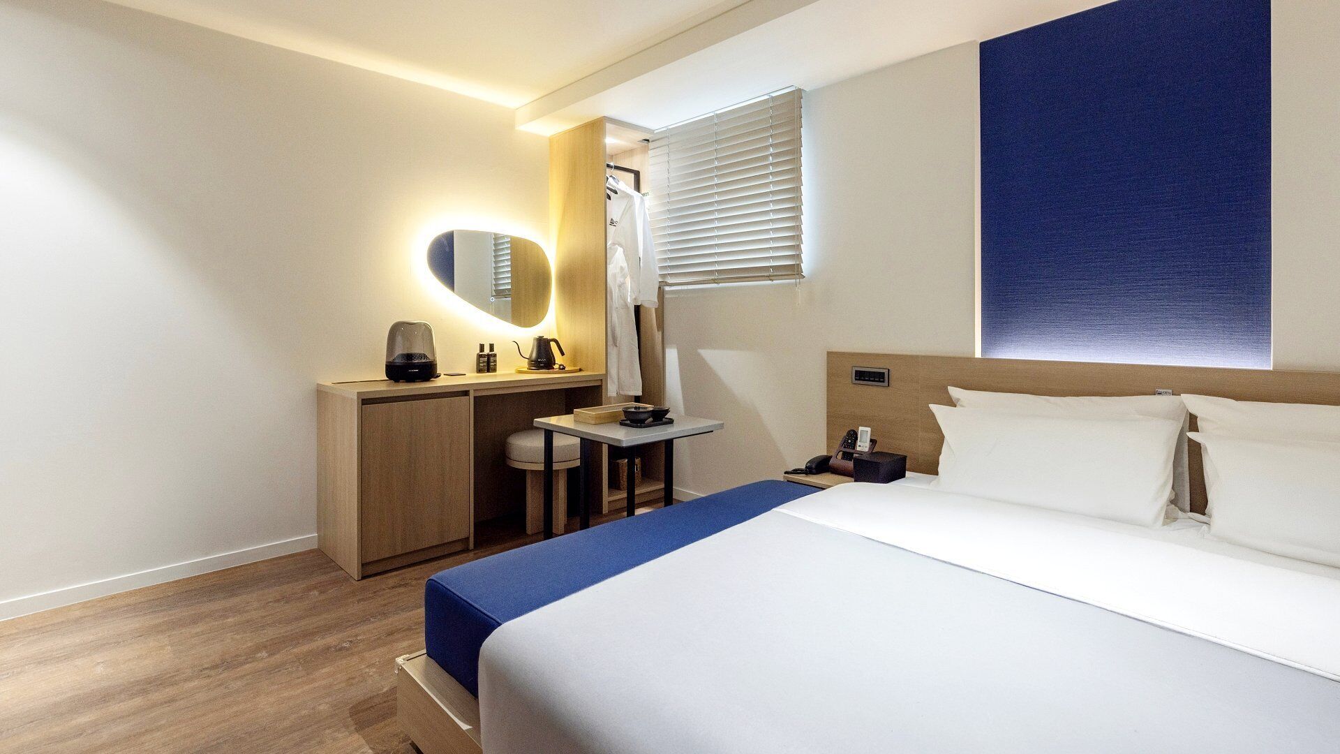 Une chambre d’hôtel comprenant un lit, un bureau, un miroir, une fenêtre avec stores et une œuvre d’art accrochée au mur.