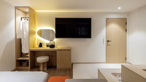 Ein modernes Hotelzimmer mit einem Holztisch, einem kleinen Hocker, einem Bett, einem Kleiderschrank und einem flachbildschirmfernseher an der Wand.